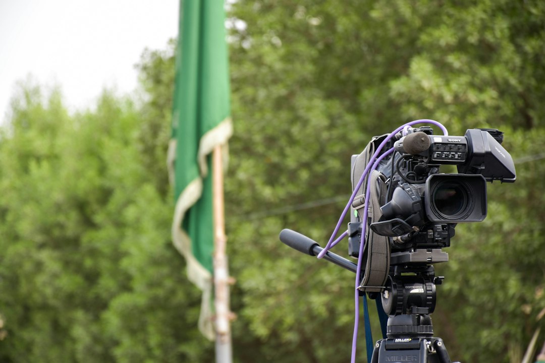 black video camera on tripod in front of green flag