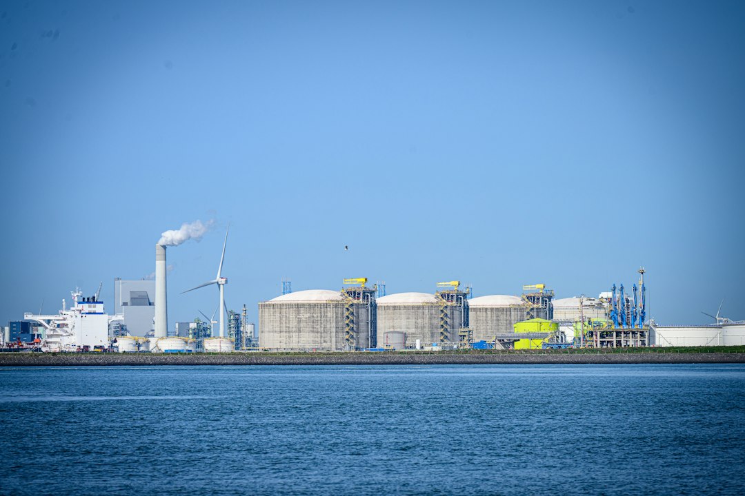 Industrial complex with tanks, factory, and wind turbines by water.
