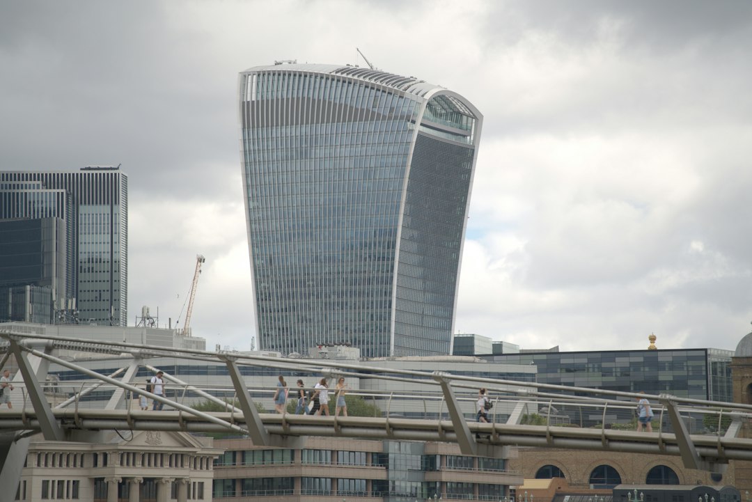Modern skyscraper and pedestrian bridge under a cloudy sky.